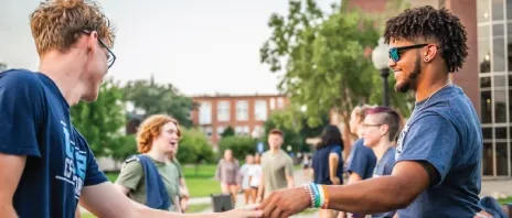 Students shaking hands outside at a campus event.