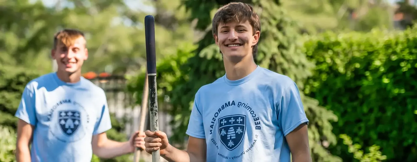 Two students holding yard work equipment while volunteering in the community